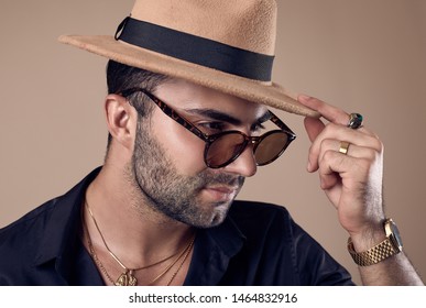 Studio portrait of a beautiful brutal tanned hipster man in a black shirt, hat and glasses