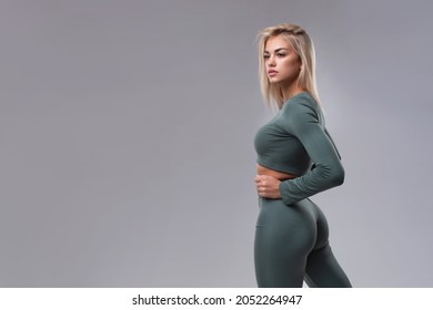 Studio portrait of a beautiful girl with big buttocks in sportswear on a gray background.