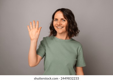 Studio portrait of a beautiful mature smiling woman waving at the camera over grey background. - Powered by Shutterstock