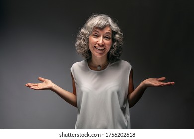 Studio portrait of a beautiful smiling middle-aged woman with gray hair and a gesture of doubt with her arms