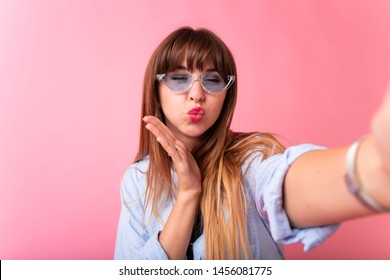 Studio portrait of beautiful woman smiling with white teeth and making selfie, photographing herself over pink background. Girl Taking Selfie Picture With Duck Face Lips Smart Phone Photo 
