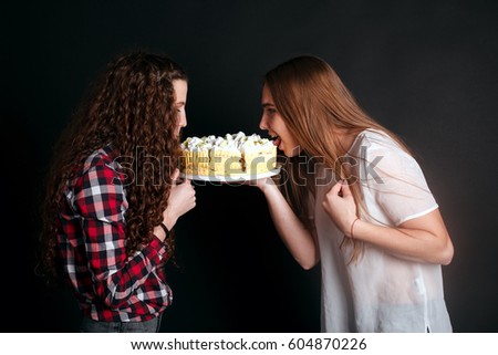 studio portrait of Beautiful young caucasian women girls sisters best friends bff isolated on black background, laughing, playing the fool, act the ass goofy eating cake smearing each other with cream