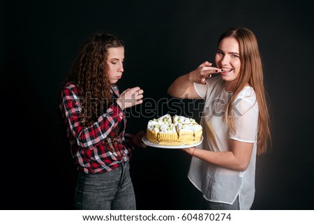studio portrait of Beautiful young caucasian women girls sisters best friends bff isolated on black background, laughing, playing the fool, act the ass goofy eating cake smearing each other with cream