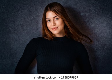 Studio Portrait Of Beautiful Young Woman Looking At Camera And Smiling While Standiing At Isolated Dark Background. 