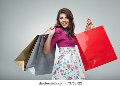 studio portrait of a beautiful young woman, in a colourful outfit, holding in her hands a few shopping bags. she is laughing and looking very happy.