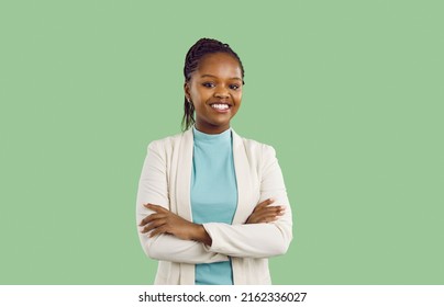 Studio portrait of black businesswoman with toothy smile. Confident good looking young woman with Afro braids, in white jacket and mint turtleneck standing isolated on solid green colour background
