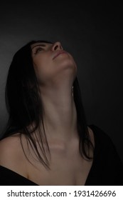 Studio portrait of a brunette in black clothes on a dark background,her head tilted back
