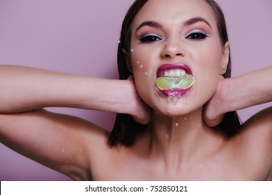Studio portrait of caucasian female model with squeezing lemon with her mouth in pink lip stick