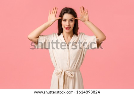 Studio portrait cheerful and carefree playful brunette female in dress, showing funny gestures, scolding someone looking happy and goofy, mimicking playfully, standing pink background