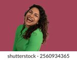 Studio portrait of cheerful young latin woman with curly hair wearing green long sleeve shirt, laughing with open mouth showing her teeth