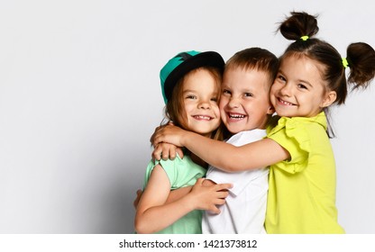 Studio portrait of children on a light background: full body shot of three children in bright clothes, two girls and one boy. Triplets, brother and sisters. hugging on camera. Family ties, friendship.