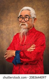 Studio Portrait Of Chinese Old Man Wearing Eyeglasses With White Hair And Beard In Tradional Chinese Clothing On Studio Backdrop Background