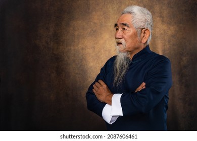 Studio Portrait Of Chinese Old Man With White Hair And Beard In Traditional Chinese Clothing On Studio Backdrop Background