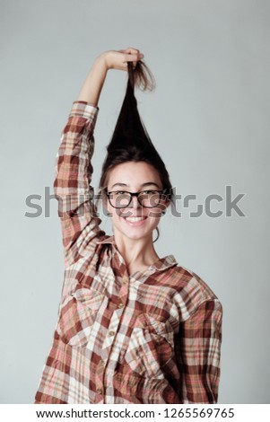 A studio portrait of a cute young brunette girl in lumbercheck check shirt playing with hair