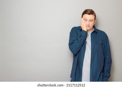 Studio portrait of disappointed mature man making facepalm gesture, expressing bewilderment, frustration and shock, wearing casual blue shirt, standing over gray background, with copy space