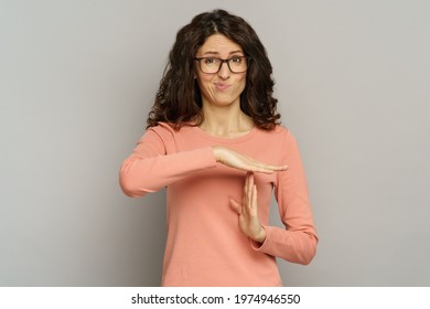 Studio portrait of dissatisfied embarrassed woman show timeout hand gesture. Tired casual business female in eyeglasses need break time out of work. Shot of frustrated businesswoman over gray wall