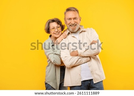 Studio portrait of elderly couple posing on yellow background, senior handsome man and pretty woman embracing, smiling at camera