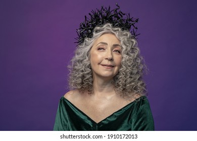 Studio Portrait Of An Elderly Woman 60-65 Years Old In A Beautiful Long Green Dress With A Crown On Her Head On A Colored Background. Concept: Stylish Pensioners Of Model Appearance, Active Life.