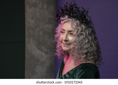 Studio Portrait Of An Elderly Woman 60-65 Years Old In A Beautiful Long Green Dress With A Crown On Her Head On A Colored Background. Concept: Stylish Pensioners Of Model Appearance, Active Life.