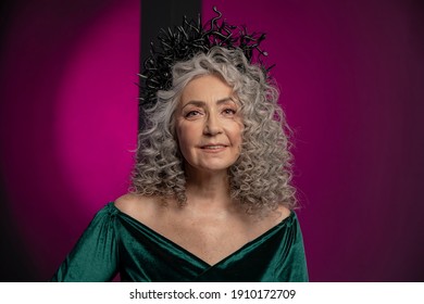 Studio Portrait Of An Elderly Woman 60-65 Years Old In A Beautiful Dress With A Crown On Her Head On A Colored Background. Concept: Stylish Pensioners Of Model Appearance, Active Life.