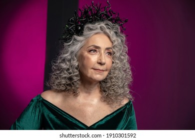 Studio Portrait Of An Elderly Woman 60-65 Years Old In A Beautiful Dress With A Crown On Her Head On A Colored Background. Concept: Stylish Pensioners Of Model Appearance, Active Life.