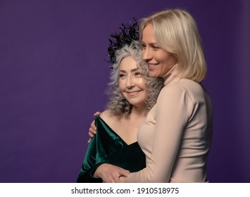 Studio Portrait Of An Elderly Woman 60-65 Years Old Embracing A Young Woman 25-30 Years Old On A Colored Background. Concept: Stylish Retirees Of Model Appearance And Young People, Active Lifestyle, 