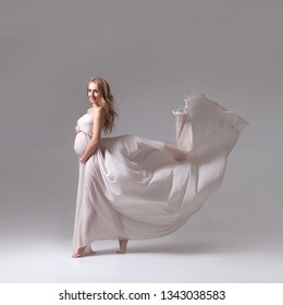 Studio portrait of elegant pregnant woman in a white flying dress on white background