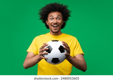 Studio portrait of excited young african american football fan man with the ball in hands smiling being happy to support favorite team. Isolated over green background. - Powered by Shutterstock