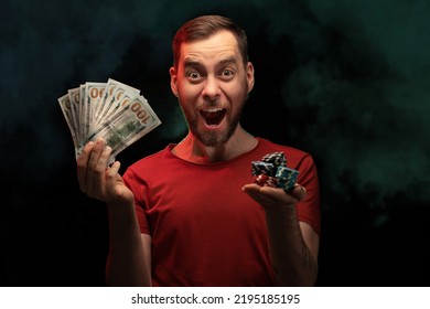 Studio Portrait Of Excited Young Man Posing With A Stack Of Poker Chips And Ward Of Dollar Banknotes In Hands Over Black Background With Smoke Effect. Gambling, Sport Betting, Poker, Casino Concept.