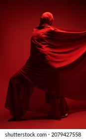 Studio Portrait Of An Expressive Female Fashion Model Wrapped In Red Fabric Posing On A Red Background. High Fashion Shoot. 