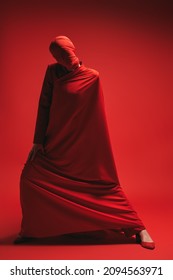 Studio Portrait Of An Expressive Female Fashion Model Wrapped In Red Fabric Posing On A Red Background. High Fashion Shoot. 