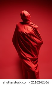 Studio Portrait Of An Expressive Female Fashion Model Wrapped In Red Fabric Posing On A Red Background. High Fashion Shoot.  