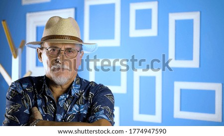 Studio portrait of an fashion old man in summer hawaiian shirts and straw hat looking at camera on a colorful wall. Concept of human emotions, facial expression. 