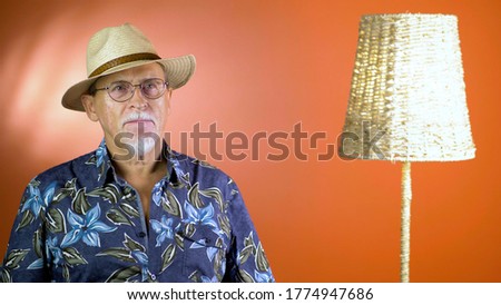 Studio portrait of an fashion old man in summer hawaiian shirts and straw hat looking at camera on a colorful wall. Concept of human emotions, facial expression. 