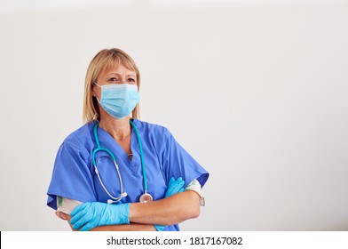 Studio Portrait Of Female Nurse Wearing Scrubs And PPE Face Mask And Gloves Against White Background