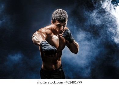 Studio Portrait Of Fighting Muscular Man In Smoke On Blue Background