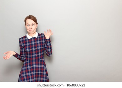 Studio Portrait Of Funny Confused Perplexed Blond Girl Wearing Checkered Dress, Making Silly Goofy Faces, With Crossed Eyes, Looking Like Stupid Person, Standing Over Gray Background, With Copy Space