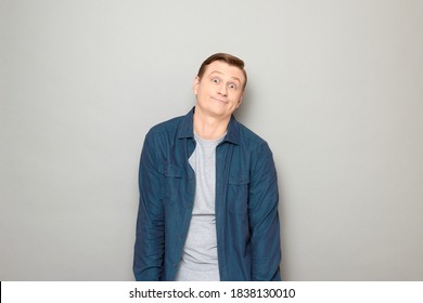 Studio Portrait Of Funny Puzzled Mature Man Wearing Shirt, Shrugging Shoulders, Smiling, Making Goofy Clueless Face, Not Understanding What Happened, Standing Over Gray Background