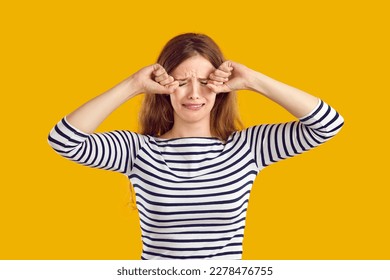 Studio portrait of a funny sad crying young woman. Pretty girl isolated on a yellow background feeling very upset and unhappy, crying and rubbing her eyes