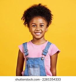 Studio portrait of girl looking standing alone isolated against a yellow background. Cute hispanic child posing inside. Happy and cute kid smiling and looking carefree in casual clothes