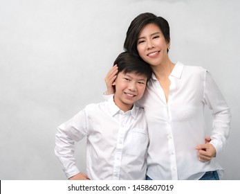 Studio Portrait Of A Good Looking Asian Preteen Boy And His Beautiful Mom In White Shirt Holding Each Other And Smiling Happily To Camera. Mother's Day, Parenting Teen, Mother And Son Concept.