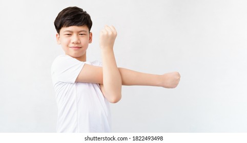 Studio portrait of a good looking, friendly, sporty, fit and healthy asian teenage boy with confident smile. He standing and do basic arms and shoulders stretching. Teen physical activity, Isolated.