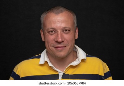 Studio Portrait Of A Gray-haired Man 40-45 Years Old In A Yellow T-shirt On A Dark Background. Perhaps He Is Just A Buyer, An Actor Or A Truck Driver, A Loader Or A Military Pensioner