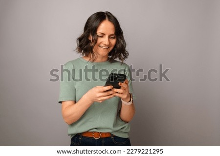 Studio portrait of a handsome good looking mid age woman is using phone over gray backdrop.