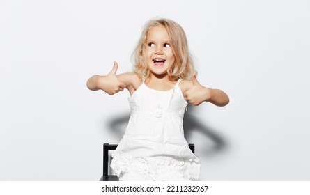 Studio Portrait Of Happiness Child Girl With Blonde Hair Showing Thumbs Up, Looking Away On White Background.