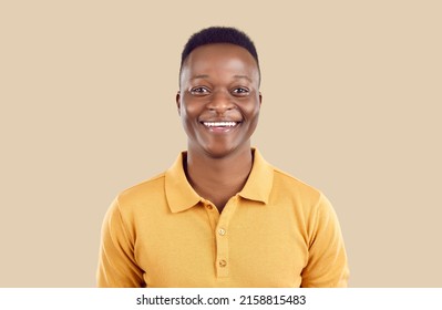 Studio portrait of happy African American man. Cheerful joyful handsome young guy in polo shirt standing on beige background, looking at camera and smiling - Shutterstock ID 2158815483