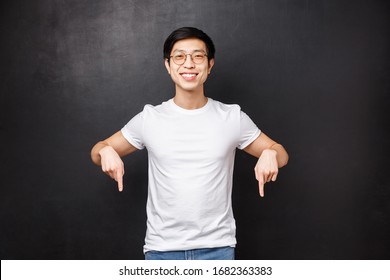 Studio Portrait Of Happy Handsome Asian Male Student In White T-shirt, Inviting New Members Join His Team Start Career In Business, Pointing Fingers Down Look Here Sign, Smiling Camera