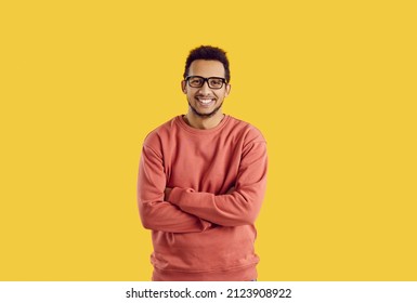 Studio Portrait Of Happy Male College Or University Student. Handsome Young Black Man In Glasses Standing With His Arms Folded Isolated On Color Background, Smiling And Looking At Camera