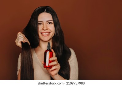 Studio Portrait Of Happy Satisfied Woman Holding Her Long Healthy Brown Hair And Showing At Camera Shampoo Or Conditioner, Female Using Natural Paraben Free Hair-care Beauty Products, Selective Focus