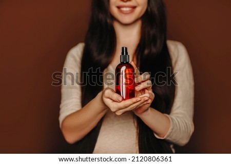 Studio portrait of happy satisfied woman holding her long healthy brown hair and showing at camera shampoo or conditioner, female using natural paraben free hair-care beauty products, selective focus